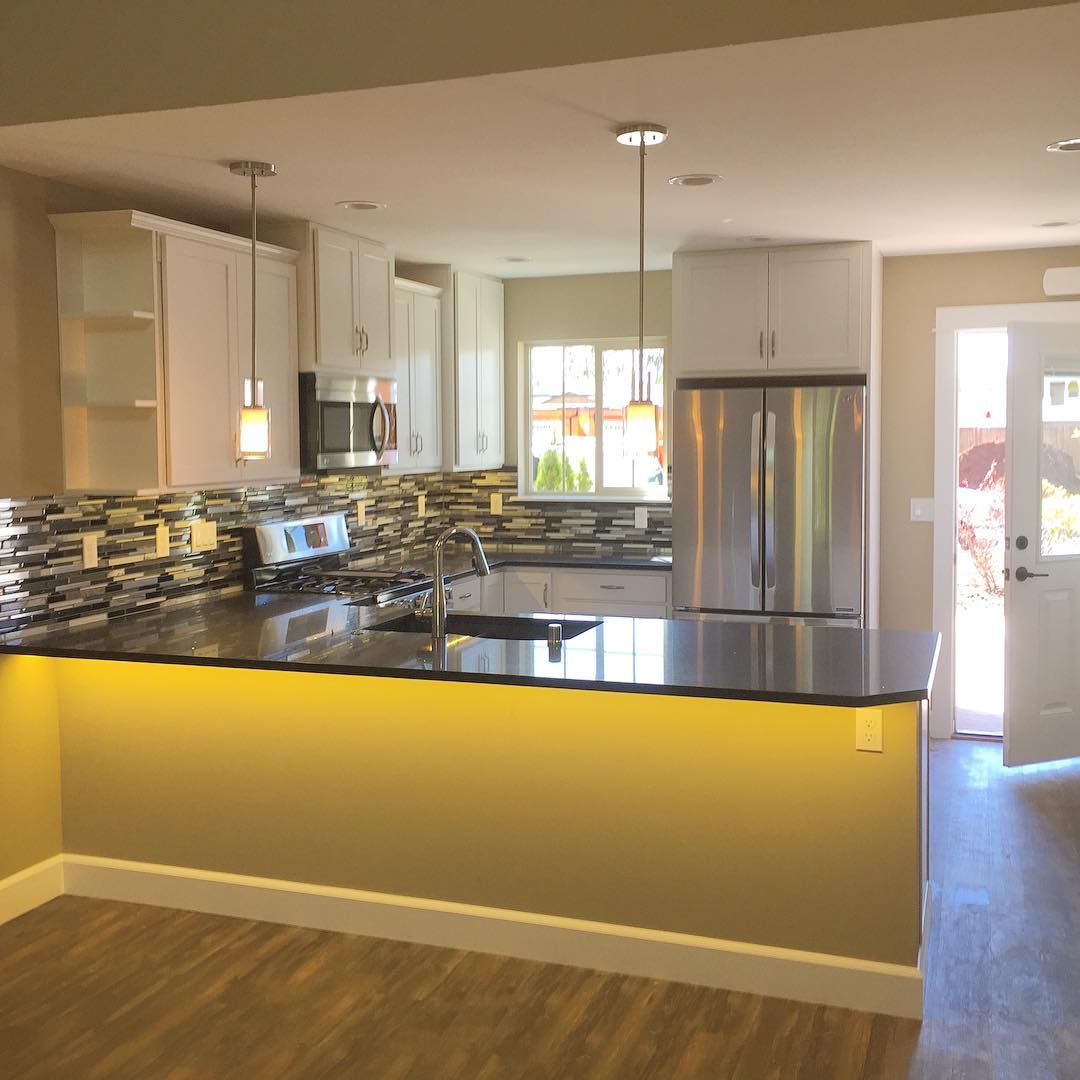 A kitchen with a stone backsplash, under-cabinet lighting and stainless appliances