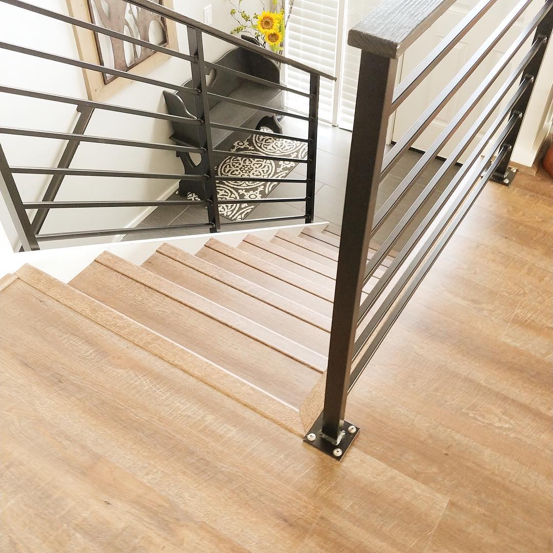 A staircase with wood treads, black metal railings and hardwood flooring