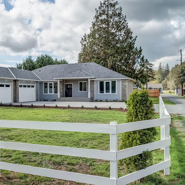 A single-story home with a white three-rail fence and open lawn